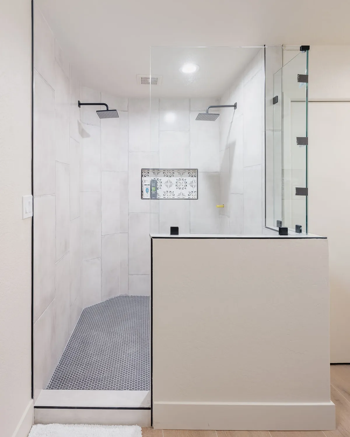 A modern en-suite bathroom featuring a glass shower enclosure with dual rainfall shower heads, textured wall tiles, and distinctive hexagonal floor tiles. The space exudes a spa-like ambiance—perfect for self-care and relaxation.