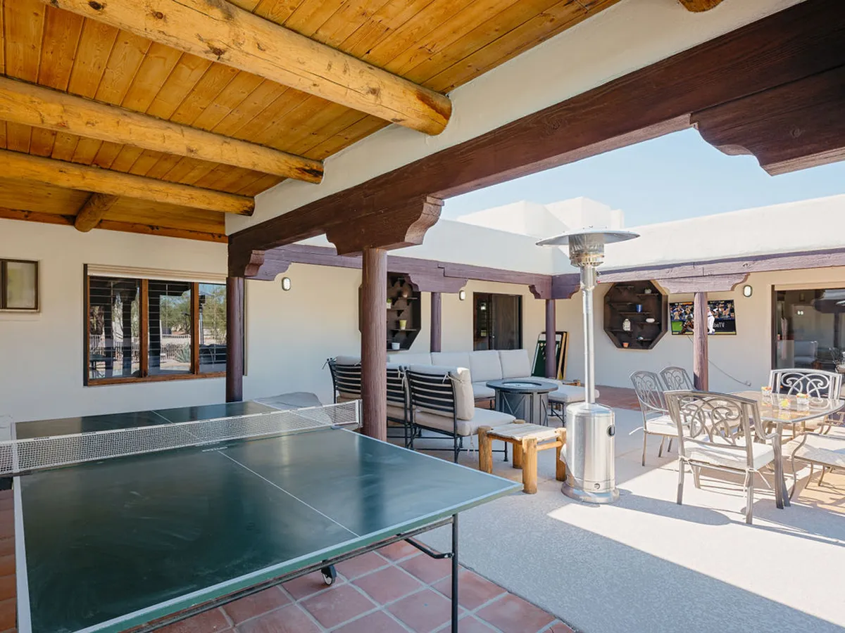 An exterior view showcasing the home's outdoor seating area, ping pong table, and a patio heater. The setting is casual and inviting, hinting at easy arrivals and group gatherings. The presence of the driveway and accessible entrance supports the idea of adventure-ready convenience for families and groups.