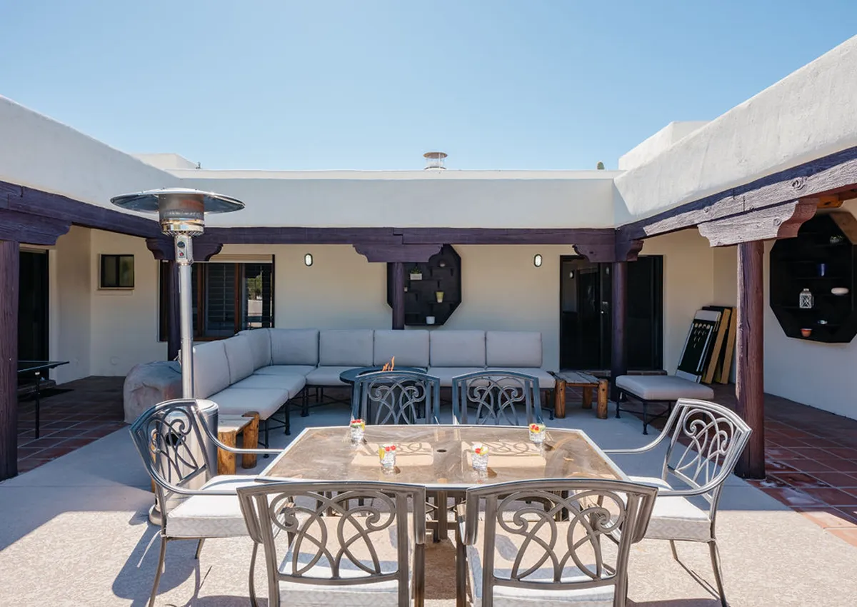 A welcoming outdoor dining area with a metal table set with decorative glasses, comfortable seating, an outdoor heater, and wall art. The setup is ideal for al fresco meals, evening drinks, or intimate conversations.