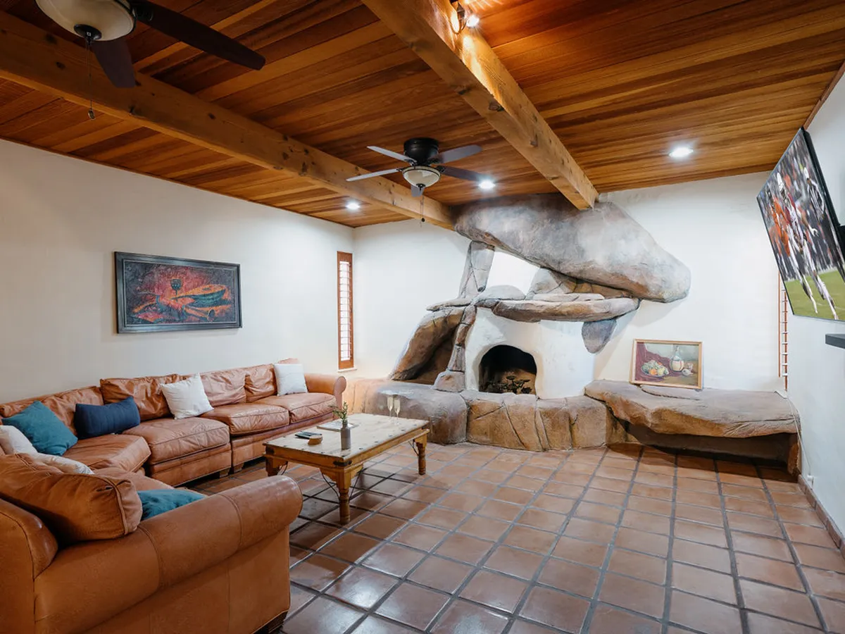 A warm, inviting interior living space featuring a stone fireplace, leather sofa, and wooden ceiling beams. The room is arranged for relaxation and group interaction, making it ideal for families or friends to unwind after exploring the outdoors.