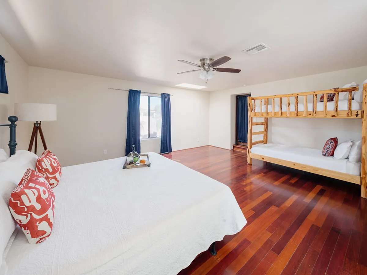 A spacious bedroom featuring a king-sized bed adorned with decorative pillows, a cozy bunk bed for children, and a large window flooding the room with natural light. The combination of adult and child-friendly sleeping spaces makes this room ideal for families seeking both comfort and flexibility.