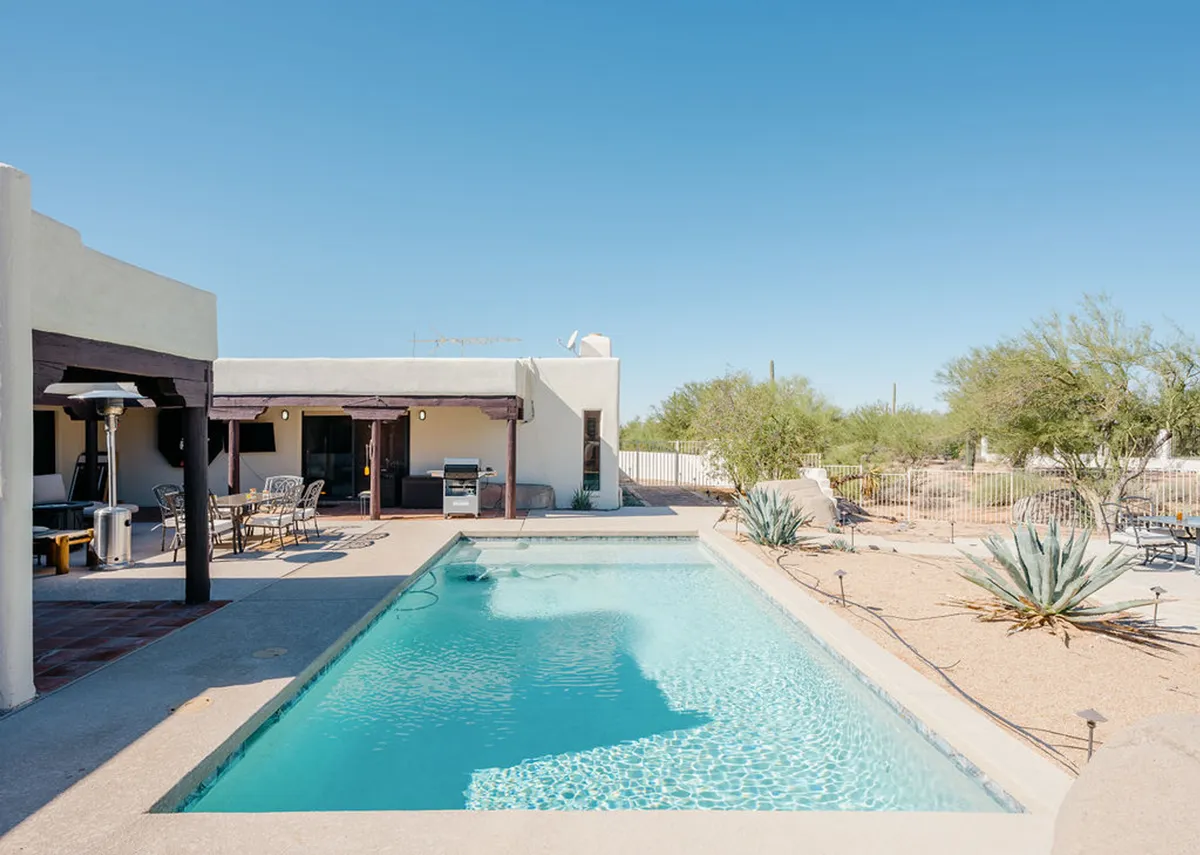 An inviting exterior image of a private swimming pool surrounded by patio furniture, a grill area, and desert landscaping. The tranquil setting is ideal for relaxing and family gatherings after a day of local adventures.