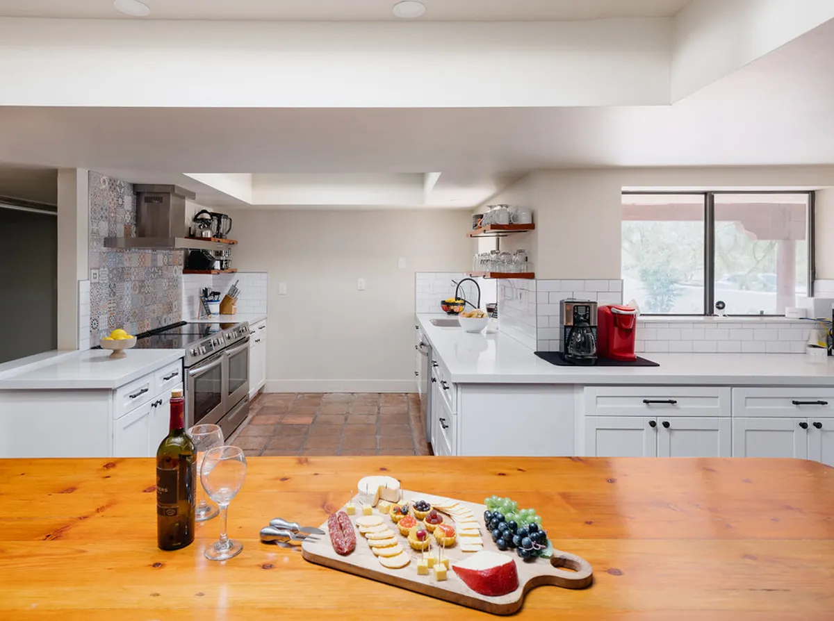 A modern kitchen with a large island at its center, set with a cheese and charcuterie board, and surrounded by sleek stainless steel appliances. The area is bright, open, and designed for social cooking and entertaining.